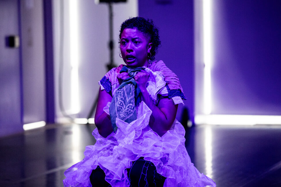 Symara sits bathed in purple light, her mouth open and eyebrows furled, clutching a bandana tightly to her chest. The image provokes a sense of urgency. Image by Maria Baranova.