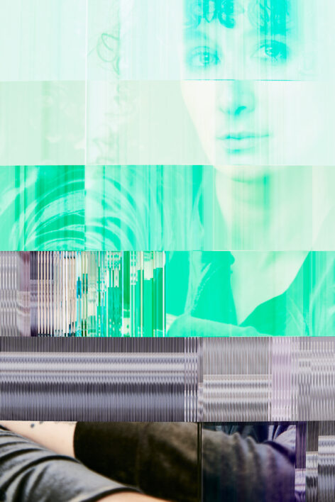 a digital photo that has a datamosh quality to it. The face of Laurel is featured mostly in shades of green, and the pixels seem to jam and striate up against one another as if the photo has been chiseled into the side of a mountain. Her arms appear at the bottom of the photo, the aspect of the image that can been seen as 