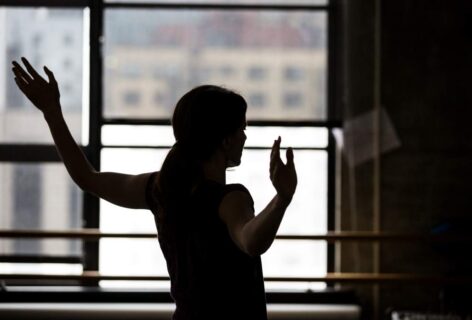 A silhouette of Jimena with her arms out in a a studio, behind her are windows and buildings. Photo by Maria Baranova