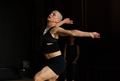 A white woman with a shaved head, wearing black shorts and a black tank top, lunges onto her right leg, arms stretched out behind her. Photo by Julia Discenza.