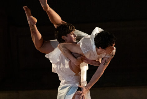 felix bryan and cove barton performing for Movement Research at the Judson Church. One dancer stands carrying the other in their arms. The other dancer arches with their feet reaching upwards. Photo by Rachel Keane.