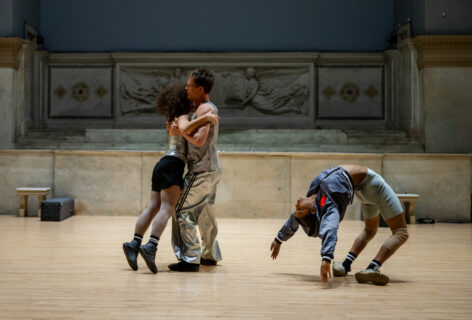 Shua Group performing for Movement Research at the Judson Church. Two dancers embrace while another is suspended in a deep back bend. Photo by Rachel Keane