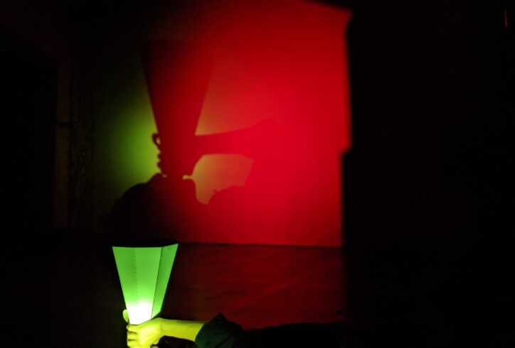 A woman is metaphorically birthing herself as she sings through a cone out of which her own shadow is revealed, in red and blue tones. Photo & light art by Lindsay Packer.