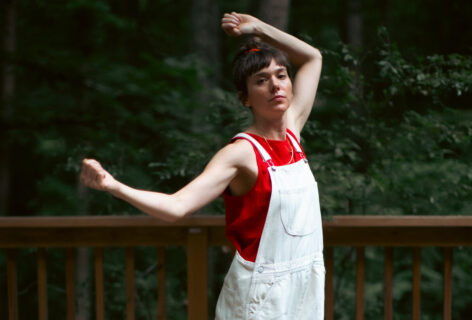 Marion dances on a deck in the woods, arms suspended in the air with her hands in fists. Photo by Anna Maynard.