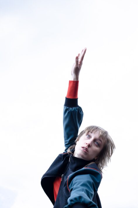 Photo of the dancer on a white background in a blue jacket with red cuffs; she looks slightly upward. Photo by Ivan Idžotić