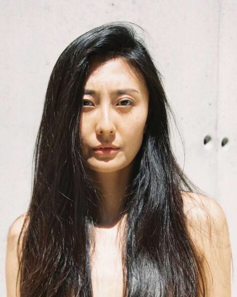 A portrait of a woman with long hair against a pale pink background. Photo by Lucrezia Pollice