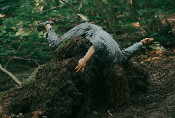 A person with long dark hair lies uprooted tree roots. Photo by Piotr Nykowski.