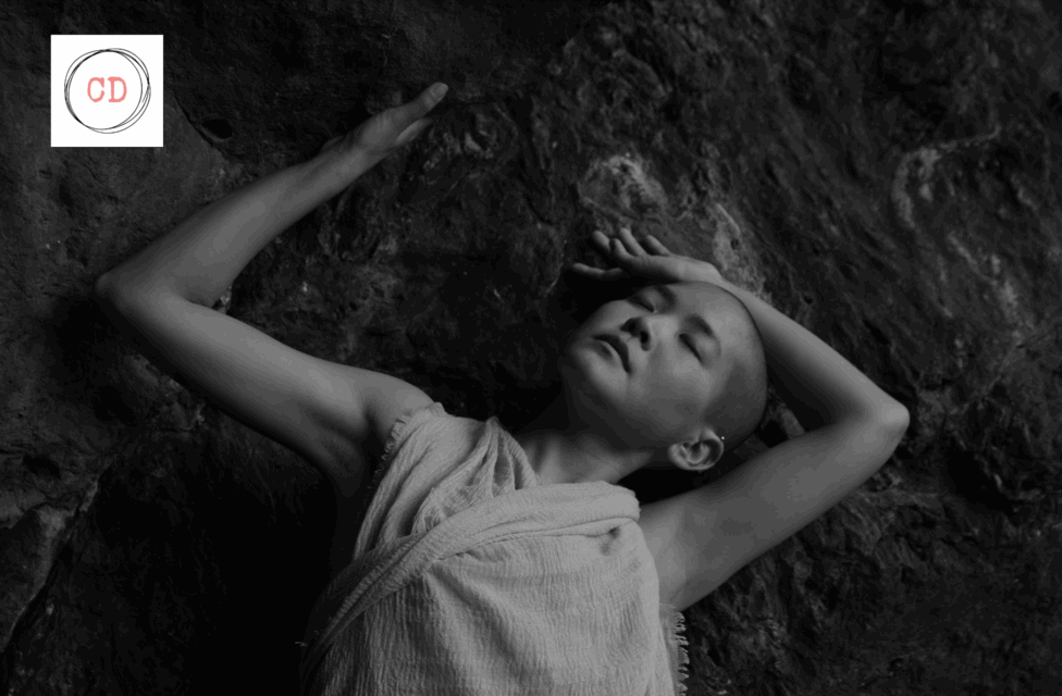 Black and white image of kyoko laying on the ground with their arms above their head. Photo by Andre Shizen.