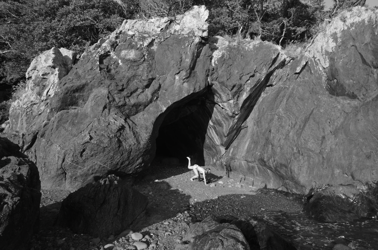 A black and white image of a rocky landscape. A small figure can be seen with their leg lifted at the base of a rock formation. Stills of the monster from the film, courtesy of the artist.