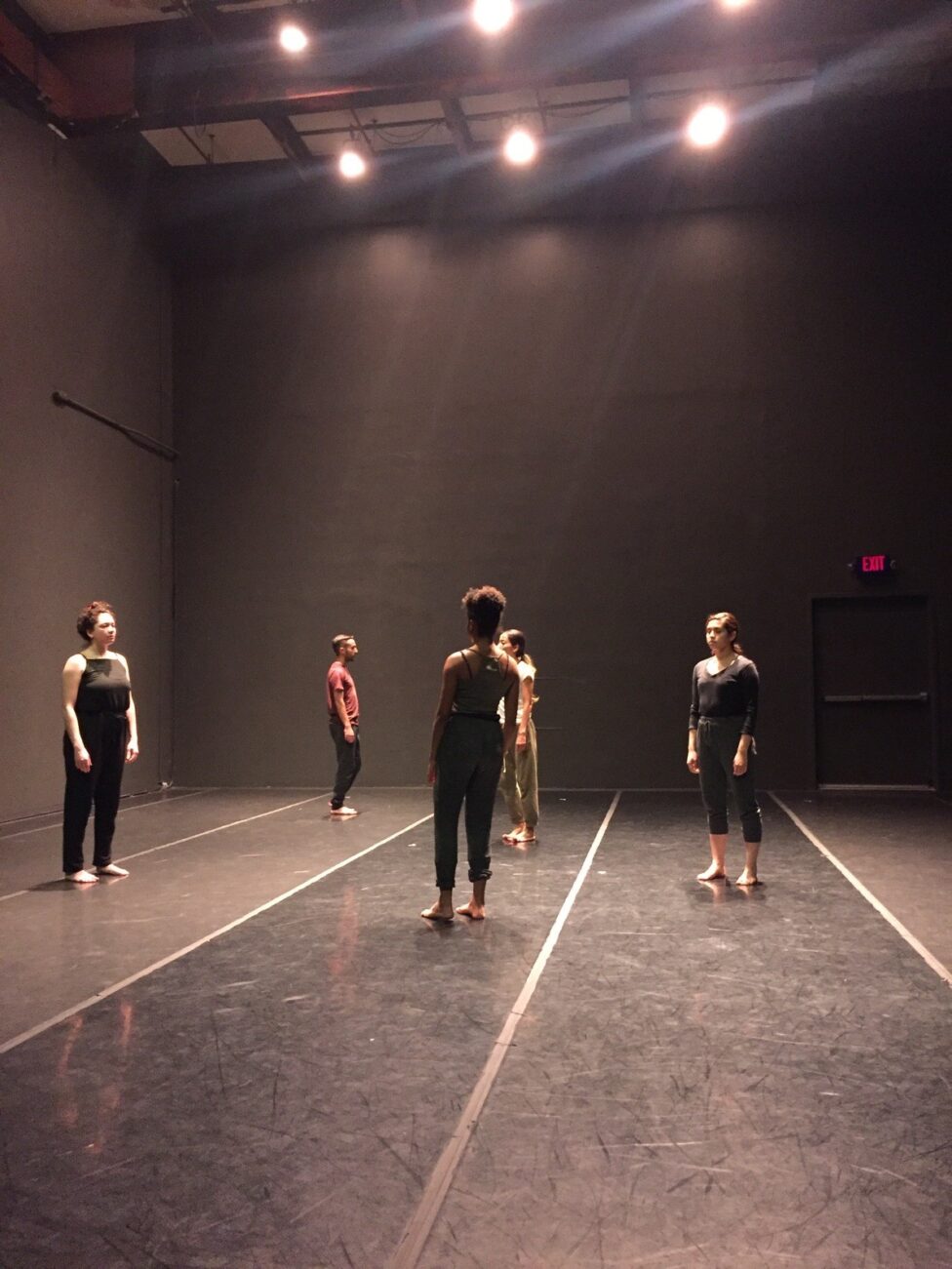 Dancers in a studio all standing in an upright position and facing one another. From