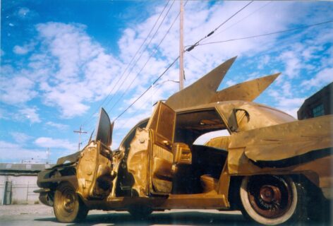 An altered Cadillac car painted gold in front of a blue sky with clouds. Vu Dan Tan's Cadillac-Icarus (1999), Courtesy of Natalia Kraevskaia.