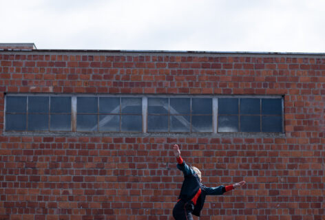 Exterior landscape consisting of a brick building in the background and a dancer in the foreground. Image by Ivan Idžotić.