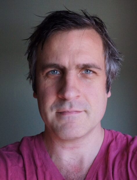 Self portrait of a white man, Peter looking directly at the camera in a red shirt. Photo by Peter Born.