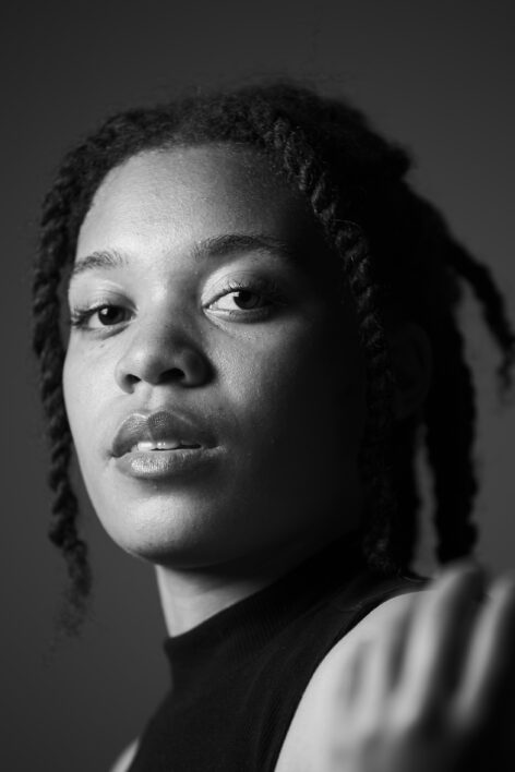 Black and white headshot of Ariana facing the camera with twists cascading down her face. Photo by Whitney Browne