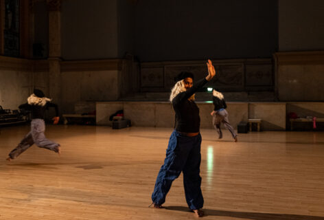 Sasha Vega's performance for Movement Research at the Judson Church. Three dancers wear blonde wigs and black berets. they move around the space. One dancer stands in the forefront a reaches. Photo by Rachel Keane.