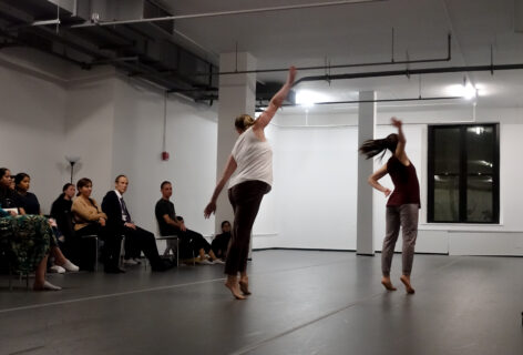 Two dancers presenting for Open Performance they stand with arms spread out. An audience watches from the side. Photo by Harry Shuanyao Zhang.