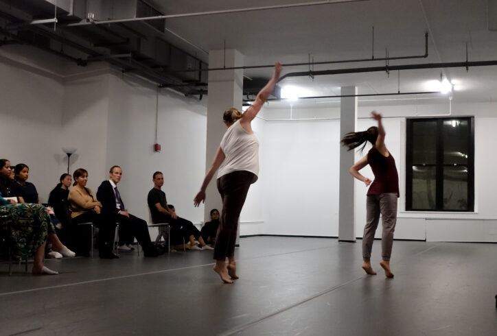 Two dancers presenting for Open Performance they stand with arms spread out. An audience watches from the side. Photo by Harry Shuanyao Zhang.