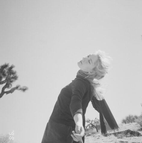 Hannah tilts back with an arm towards the camera. She is in the desert. Photo by Tatum Lenberg