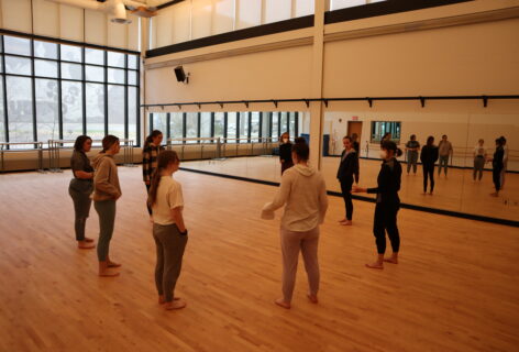 Chloë Nagle Çetinkaya teaches undergraduate dancers at the University of Wisconsin-Stevens Point. Everyone is gathered in a circle. She is on the right-hand side wearing all black with a white KN95 mask. Photo by Kevin Obsatz.
