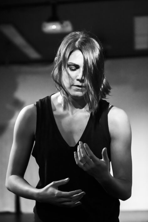 Chloë Nagle Çetinkaya, a white, cisgender person, is photographed in black and white while dancing. She gestures as if picking up something delicate, looking into her empty palms thoughtfully. Photo by Kyle Adler.