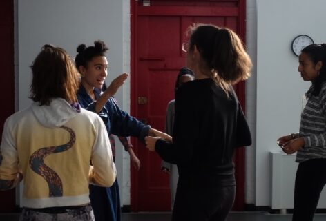 This image shows Anaïs, a mixed race woman, facilitating collective singing at Movement Research with a directive & playful gesture. Workshop participants seem focused, embodied, curious. Photo by Harry Shunyao Zhang.