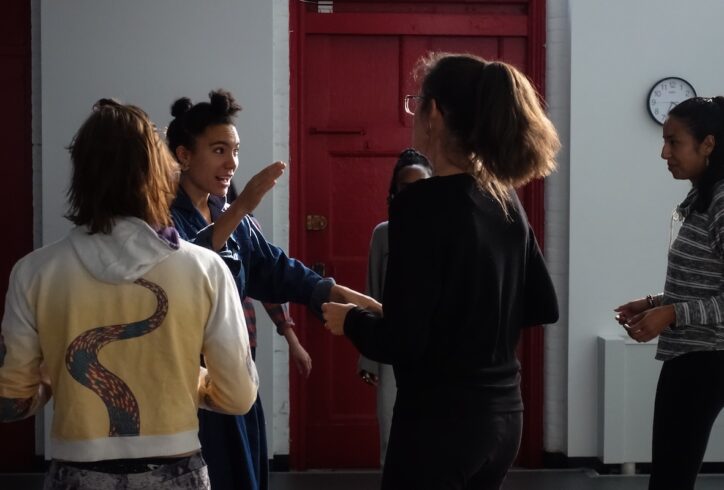 This image shows Anaïs, a mixed race woman, facilitating collective singing at Movement Research with a directive & playful gesture. Workshop participants seem focused, embodied, curious. Photo by Harry Shunyao Zhang.