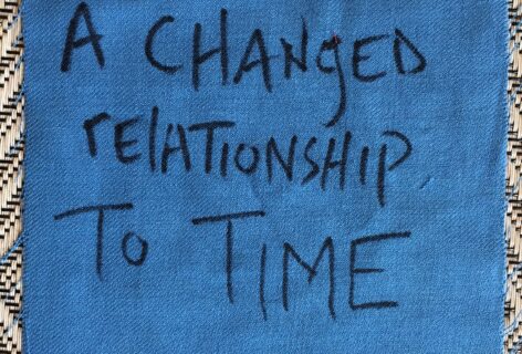 A square of blue fabric on a woven straw mat, hand-lettered in black with the words 'A changed relationship to time.