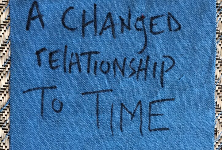 A square of blue fabric on a woven straw mat, hand-lettered in black with the words 'A changed relationship to time.