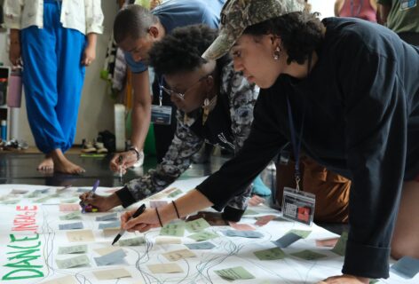 Black dancers at the BDCM Summer Untensive lean over a large floor poster, writing notes and adding sticky notes as they map their Black dance lineage together in community. Photo by Martin Nuñez-Bonilla.