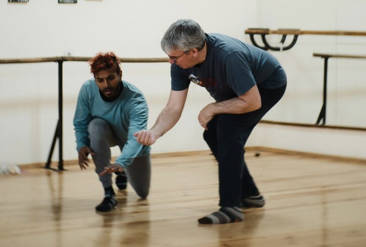 Peter Sciscioli works with a participant from a workshop in Bulgaria, both moving close to the floor, his hand cupped and the participant's hand extended while they both make vocal sound. Photo by Nikola Gyulmezov.