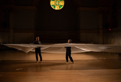 Photo from NAKA Dance Theater's piece for Movement Research at the Judson Church. Two dancers move while caught inside a billowing sheet of clear plastic. Photo by Rachel Keane.