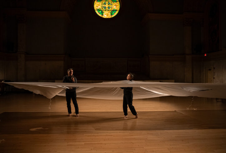 Photo from NAKA Dance Theater's piece for Movement Research at the Judson Church. Two dancers move while caught inside a billowing sheet of clear plastic. Photo by Rachel Keane.