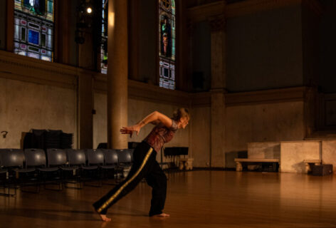 Photo from Margareta Firinger's piece for Movement Research at the Judson Church. Margareta stands in a lunge with her arms behind her. Photo by Rachel Keane.