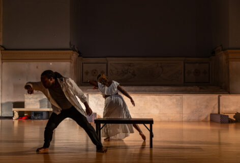 Ayo Joy Walker's piece for Movement Research at the Judson Church. Two dancers move at either side of a bench. They are in a side lunge raiding their arms to their faces. Photo by Rachel Keane.