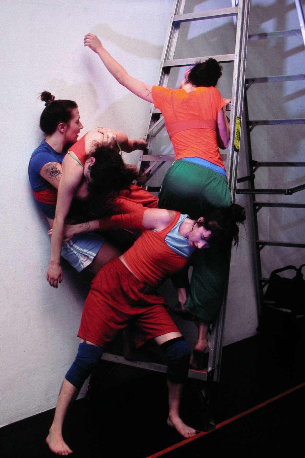 “FREE ALL NIGHT LONG”, choreographers Lena Martin and Mandolin Burns. Four bodies clad in brightly colored athletic wear climb up a metal ladder, their bodies contorting and overlapping. Photo by Noah Kentis courtesy of Highways Performance Space.