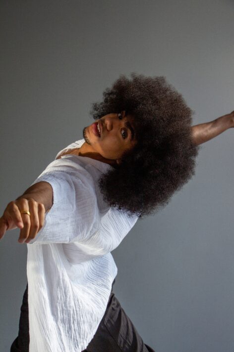 Photo of Karmel Small. He arches his back and extends his arms out. He has a large afro and brown skin. Photo courtesy of the artist.