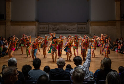 Stanley Love Performance Group performing. A large group of dancers inn colorful costumes moving together. Photo by Rachel Keane.