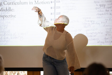 Alexis Diggs mid-gesture, standing in front of a projection screen during her Curriculum in Motion™ Institute Public Presentation. Image by Jamie Kraus.