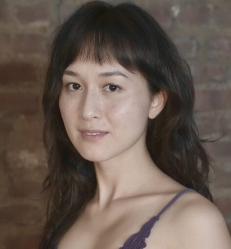 A person with long dark brown hair and bangs wearing a blue tank top.