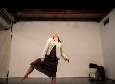 Olivia Best wearing a white long sleeved, lace top with a brown skirt. Head is cocked back while balancing on one leg and the other leg is bent. Photo by Shoshana Issacs.