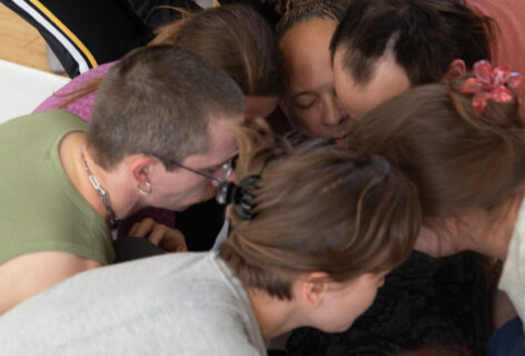A group of workshop participants gathered around a figure, caring for the figure and holding him from falling. Photo courtesy of the artist.